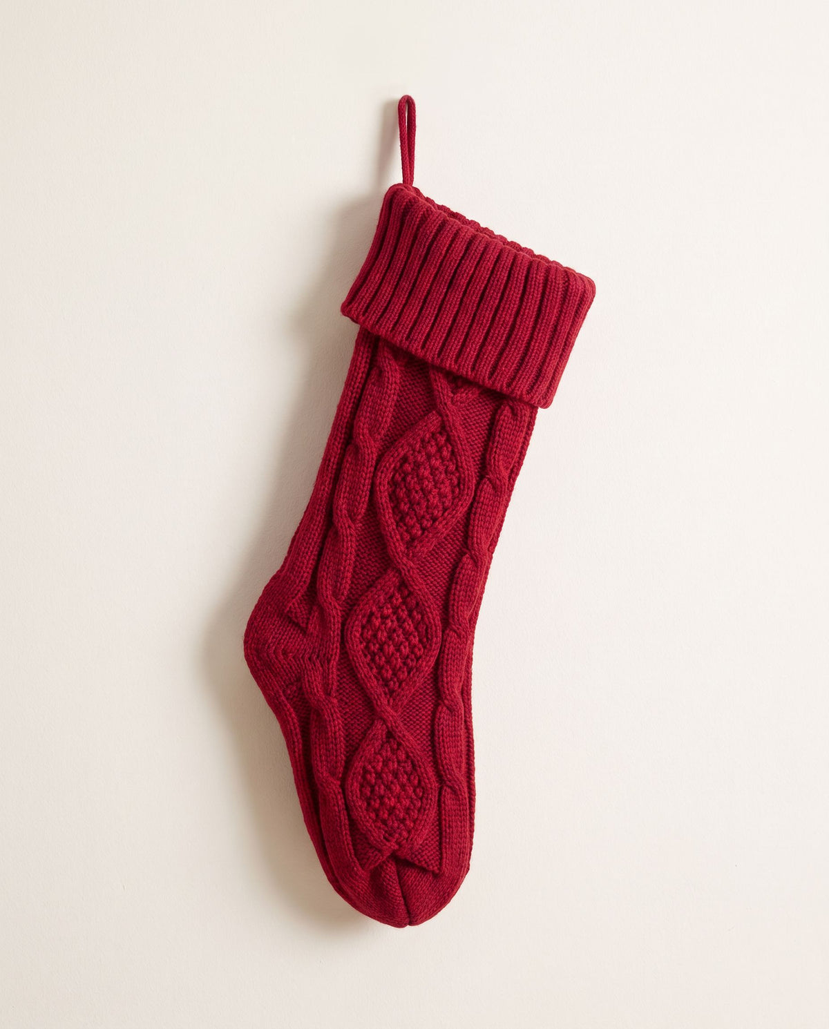 Plain red chunky cable-knit Christmas stocking with folded cuff hanging on an off-white wall