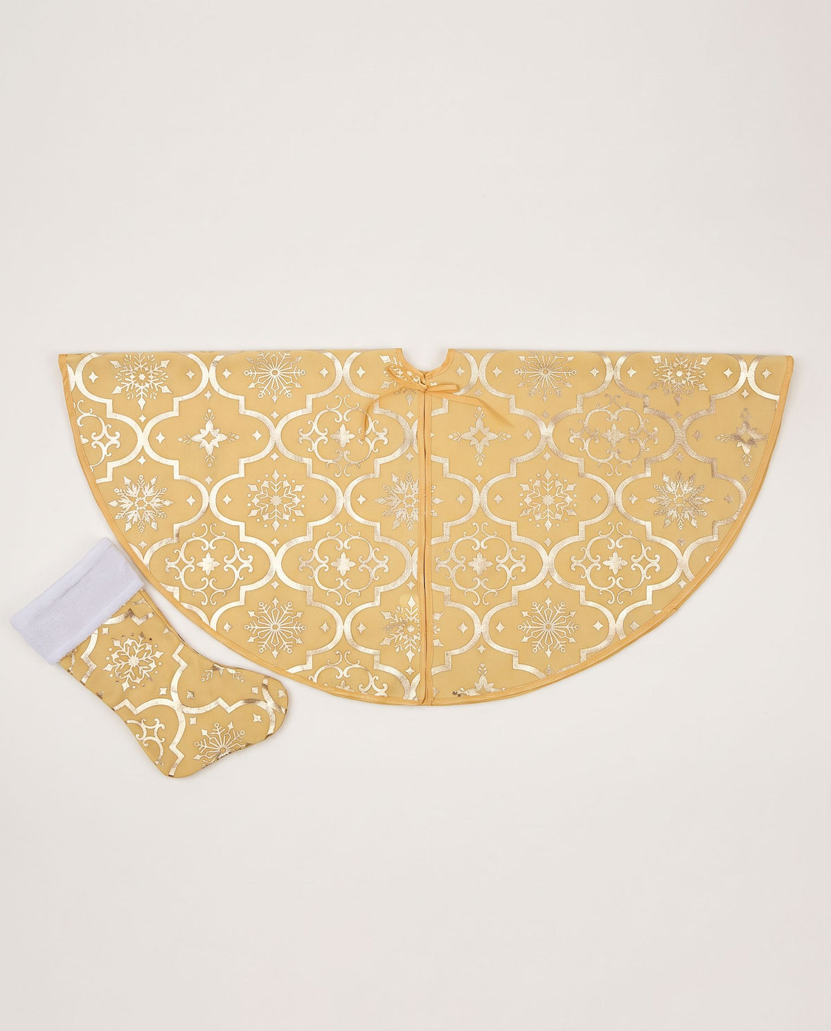 Gold Christmas tree skirt with gilded trellis and snowflake print folded in a semicircle, with a matching mini stocking