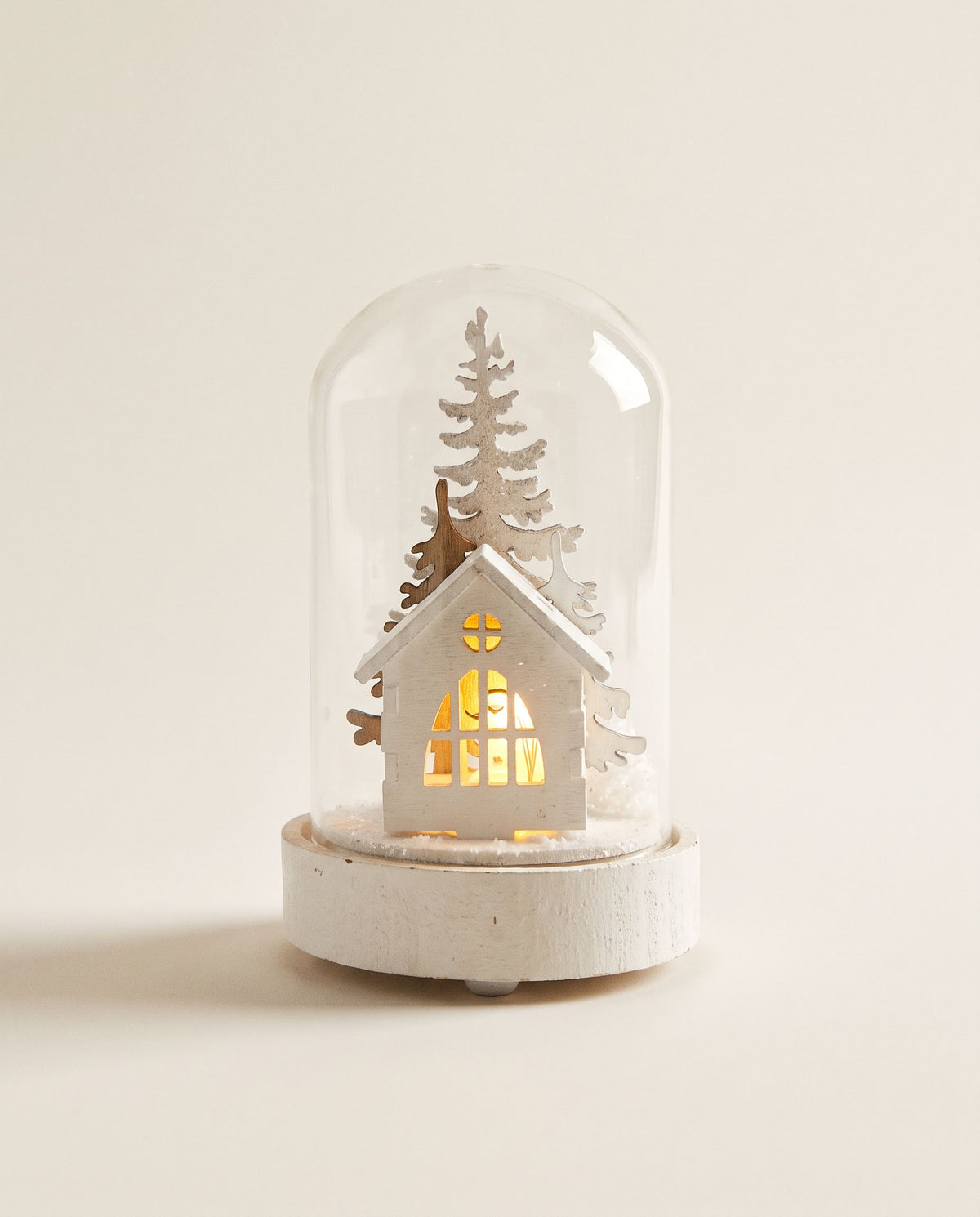 Glass dome on a white base with a white wooden house with glowing window and white snowy trees inside