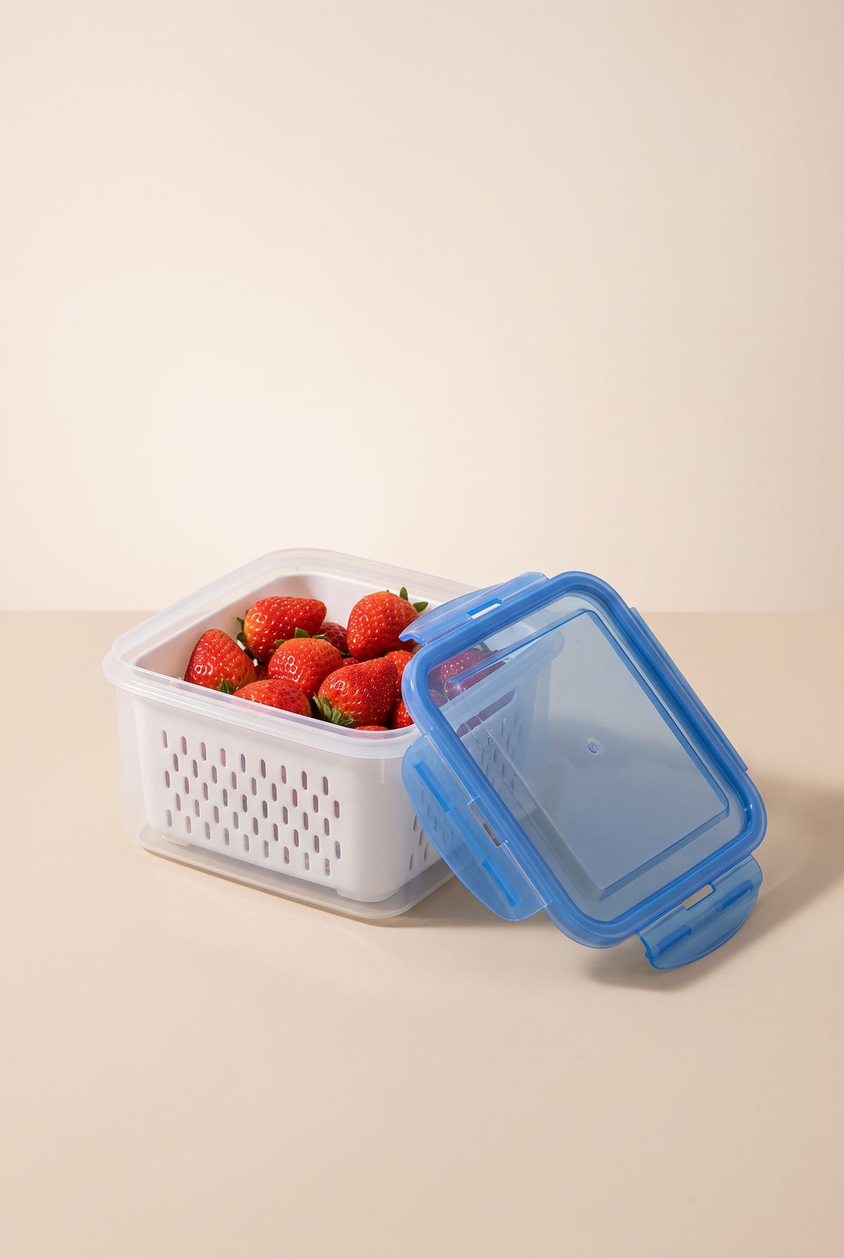 Clear FreshKeep produce container with blue lid and white drain basket holding strawberries