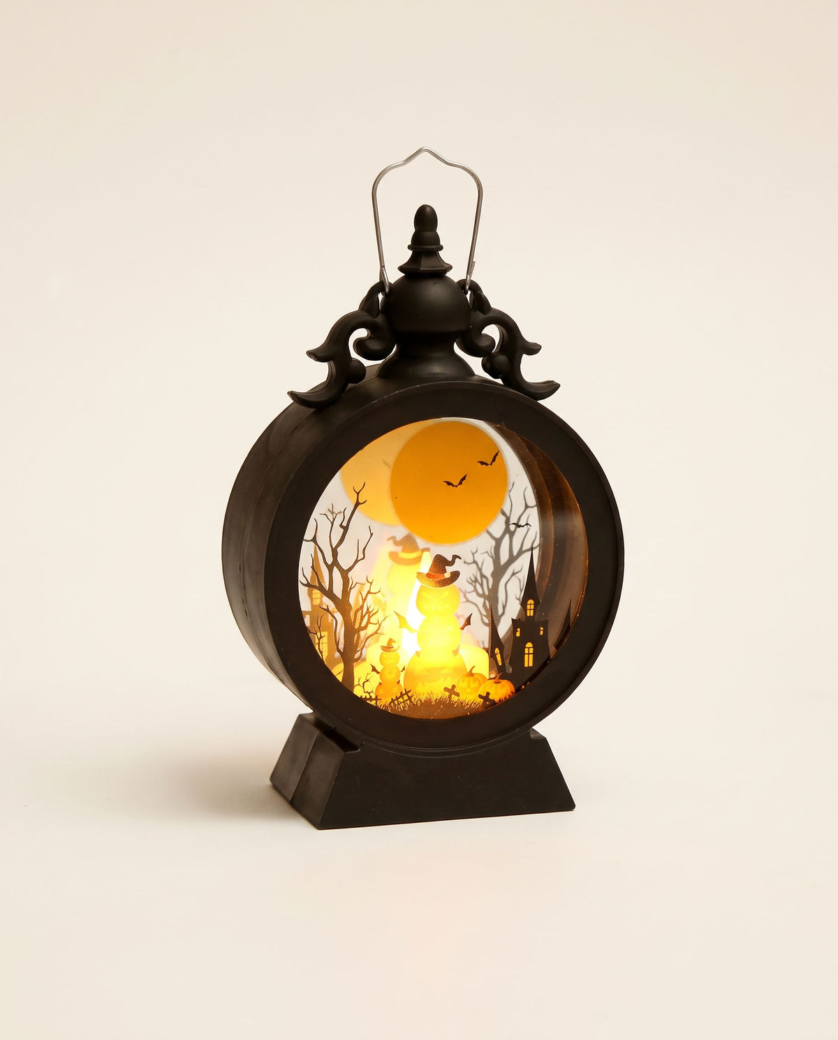 Small black Halloween lantern glowing with a cut-out orange moon, trees and jack-o'-lantern scene
