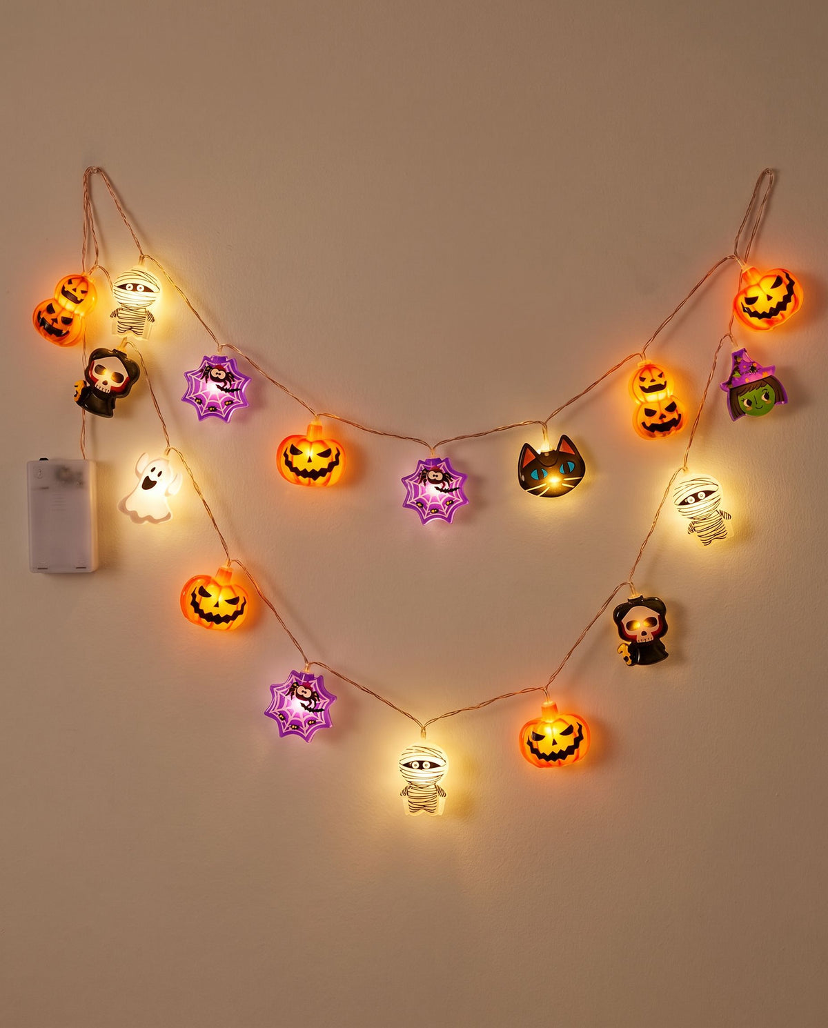 Halloween LED string lights with glowing pumpkins, ghosts and mummies draped in loops on an off-white wall