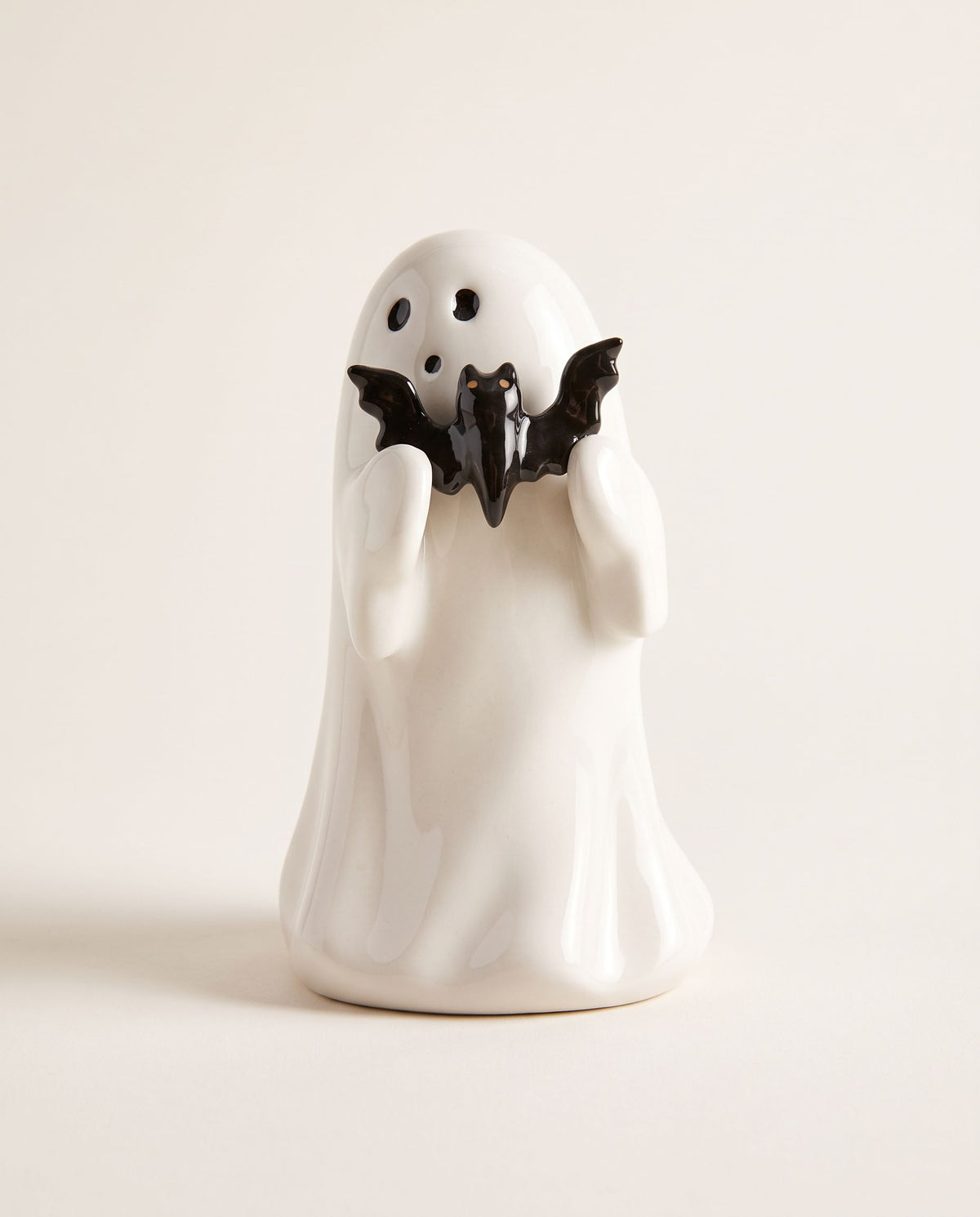 Glossy white ghost figurine holding a black bat with spread wings on an off-white background