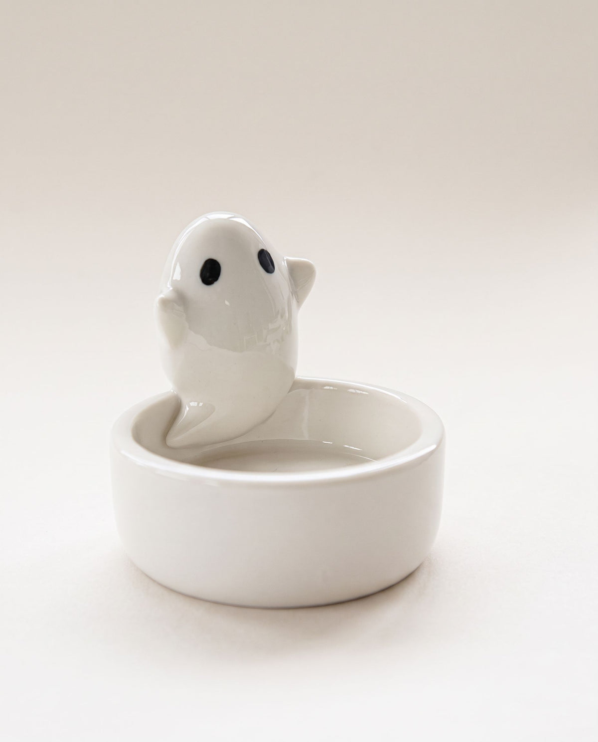 White glossy ceramic ghost leaning over an empty round tealight dish