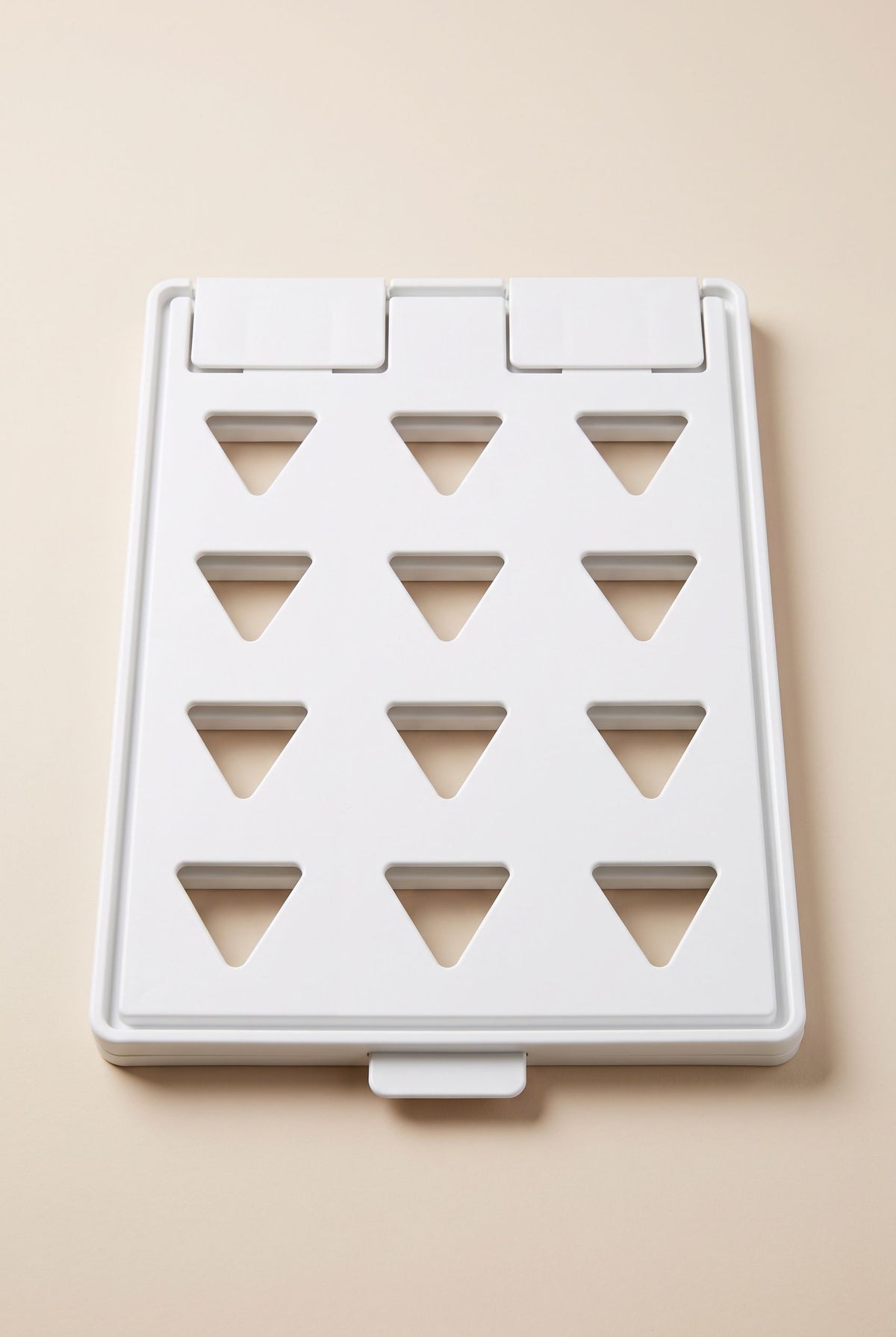 White clothes folding board lying flat and closed, twelve triangular cut-outs