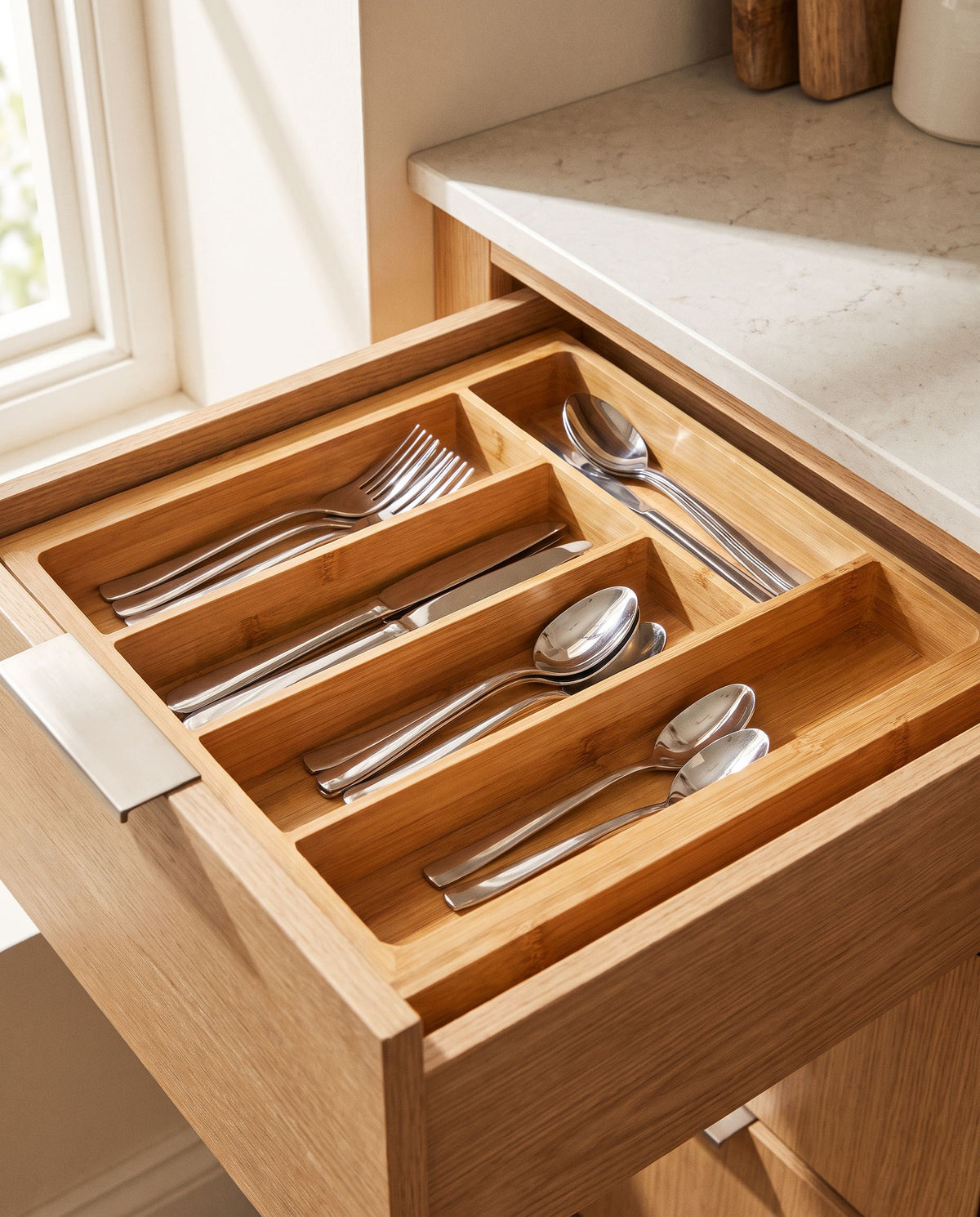 Bamboo cutlery tray seated in an open kitchen drawer holding sorted cutlery